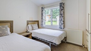 Et soveværelse med to senge, et vindue med gardiner, en radiator og en lampe i loftet.