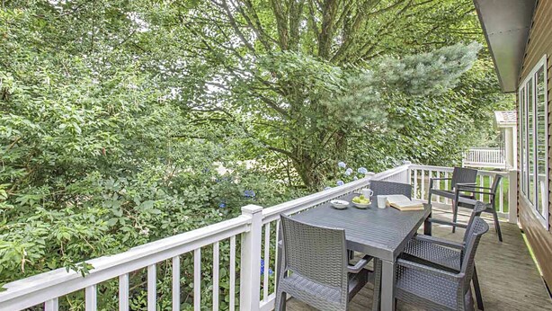 Ein Balkon mit Korbmöbeln, einem weißen Geländer und Blick auf dichtes Grün.