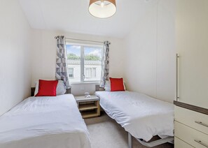 Une chambre avec deux lits, une fenêtre avec des rideaux, une table de chevet et une armoire.