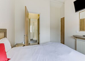Ein Hotelzimmer mit Bett, Wandfernseher und einem durchgegangenen Tür sichtbaren Badezimmer.