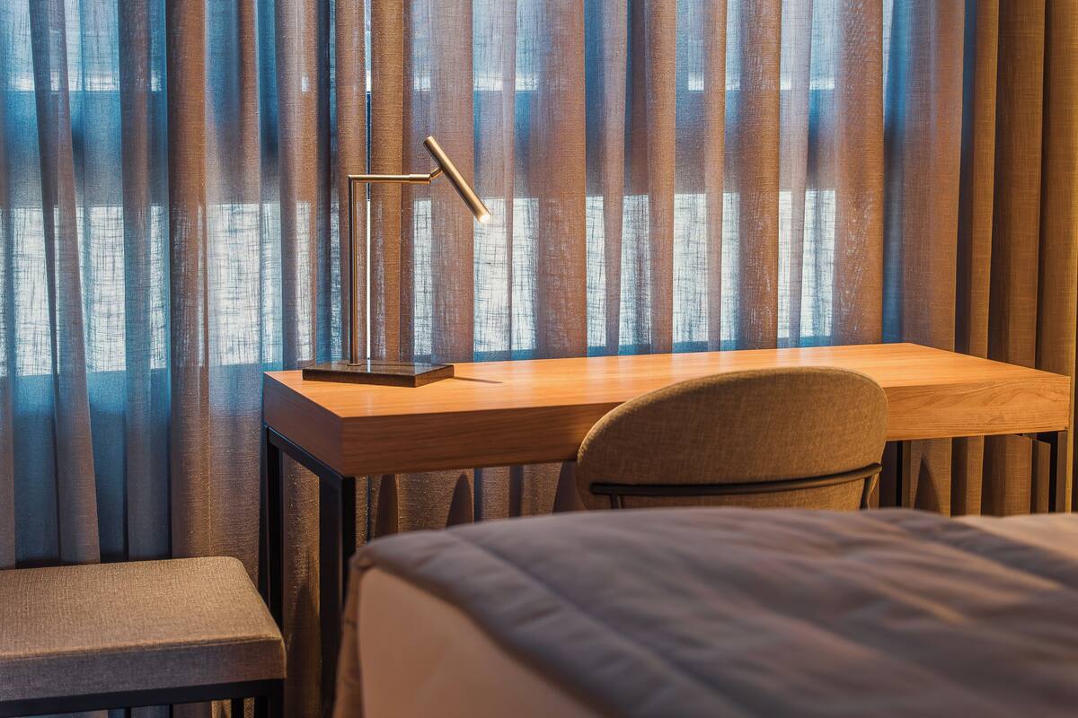 A hotel room with a wooden desk, a chair, a bed, and a window with curtains.