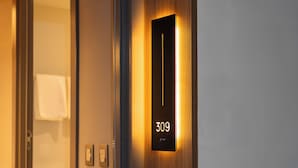 A hotel room entrance with a wooden door, a digital display showing room number 309, and a glimpse of a bathroom with a towel hanging. - Laghetto Stilo Aeroporto (Porto Alegre)