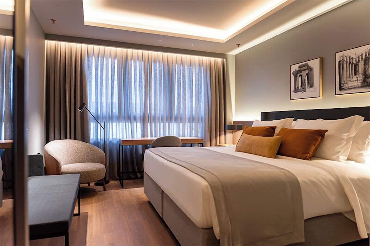 A hotel room with a bed, a desk, a chair, and a window with curtains.