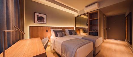 A hotel room with two beds, a desk, a chair, a large mirror, and a wardrobe.