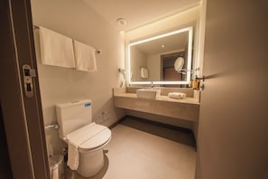 Un baño moderno con inodoro, lavamanos, espejo y dos toallas colgadas en la pared.