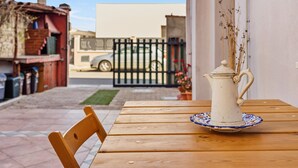 Una mesa de madera con una jarrón blanco y un plato, una silla, y una vista de un área cercada con un automóvil y un edificio al fondo.