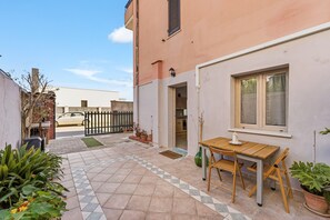 A courtyard with a wooden table and chairs, a potted plant, and a view of a car through a gate. - Casa Due Spighe San Sperate (San Sperate)