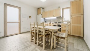 Una cocina con una mesa de comedor, sillas, armarios de madera, un refrigerador y un ventanal.