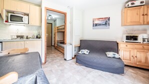 A compact living space with a kitchenette, a sofa, a bunk bed, and a microwave. - “Montagne Front De Neige” Apartment with Mountain View and Balcony (Thollon-les-Mémises)