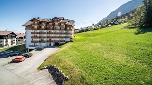 A multi-story building with a parking lot and a grassy hill in the background. - “Montagne Front De Neige” Apartment with Mountain View and Balcony (Thollon-les-Mémises)