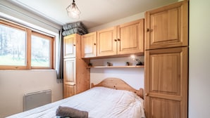 A bedroom with a bed, wooden cabinets, a radiator, and a window with a view of trees. - “Montagne Front De Neige” Apartment with Mountain View and Balcony (Thollon-les-Mémises)