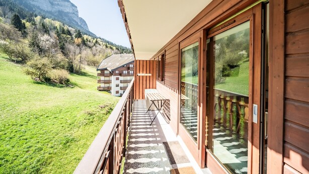 A wooden balcony with a view of a mountain and a building in the background. - “Montagne Front De Neige” Apartment with Mountain View and Balcony (Thollon-les-Mémises)