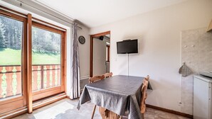 A dining area with a table, chairs, a TV, and a view of the outdoors. - “Montagne Front De Neige” Apartment with Mountain View and Balcony (Thollon-les-Mémises)