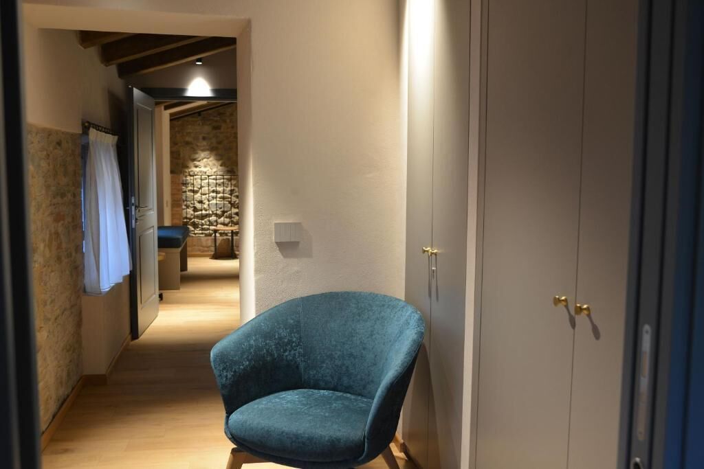 Un pasillo con una silla azul, un muro de piedra y una puerta con pomos dorados.