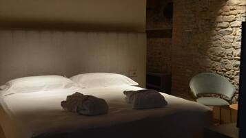 A bed with white linens and two rolled towels, a stone wall, and a light green chair.