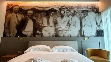 Una habitación de hotel con una cama grande, dos almohadas, una mesita de noche, una silla y una pared con una fotografía blanco y negro.