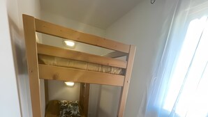 A bunk bed with a pillow and a small round stool, a window with curtains, and a wall-mounted heater. - Apartment '4-6 Couchages Proche Des Pistes' with Mountain View, Balcony and Wi-Fi (Flumet)