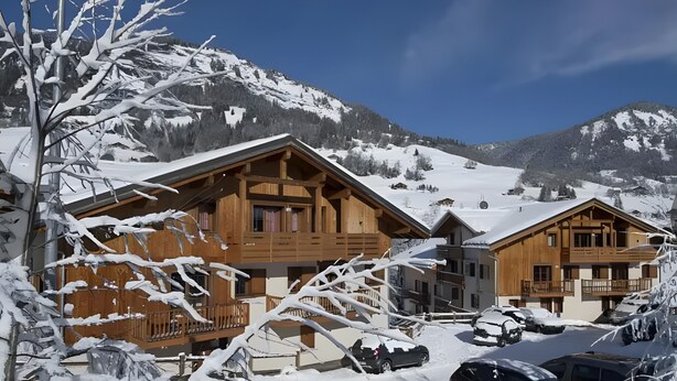 A wooden chalet with a balcony, surrounded by snow-covered mountains and parked cars. - Apartment '4-6 Couchages Proche Des Pistes' with Mountain View, Balcony and Wi-Fi (Flumet)