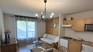 A compact kitchen with wooden cabinets, a microwave, and a dining area with a table and chairs. - Apartment '4-6 Couchages Proche Des Pistes' with Mountain View, Balcony and Wi-Fi (Flumet)