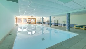 A swimming pool with clear water, surrounded by a tiled floor and walls, with a view of the outside through large windows. - Apartment '4-6 Couchages Proche Des Pistes' with Mountain View, Balcony and Wi-Fi (Flumet)