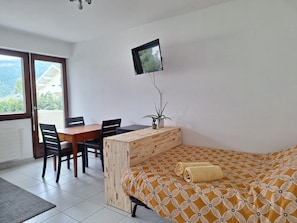 A bedroom with a bed, a desk, a chair, a TV, and a potted plant.