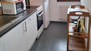 A compact kitchen with white cabinets, a microwave, a toaster, a refrigerator, and a wooden shelf with bottles. - Studio "Les Cascades" with Mountain View, Balcony, and Wi-Fi (Gaillard)