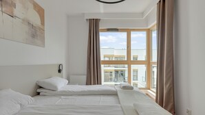 Habitació d'hotel amb un llit gran, una finestra amb cortines, un radiador i un llum penjada a la paret.