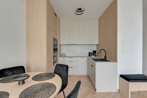 A modern kitchen with white cabinets, a marble backsplash, and a dining area with a round table and chairs. - RentPlanet - Apartament Filarskiego (Gdańsk)