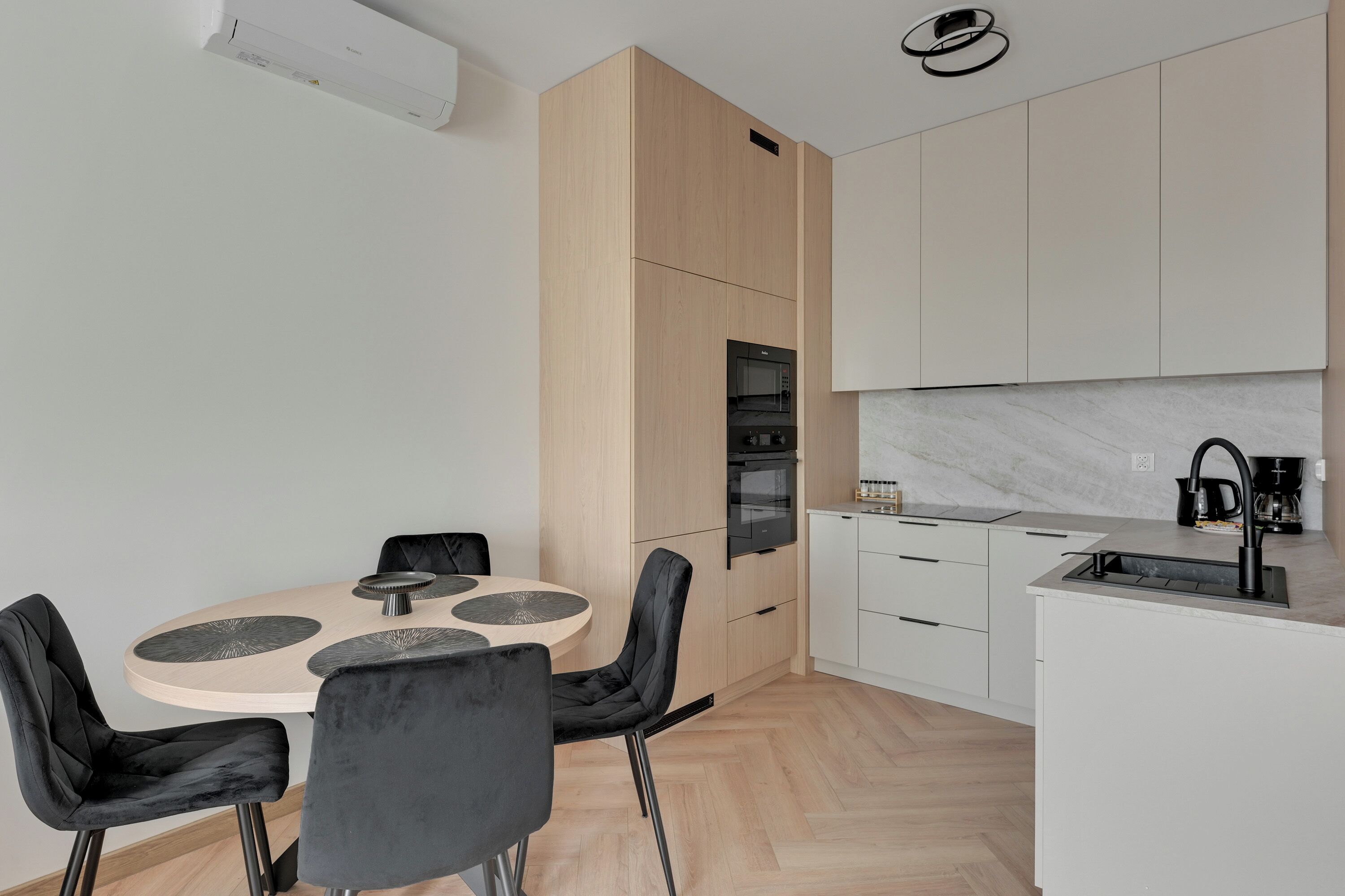 A modern kitchen with a central island, black chairs, and a dining table with a light wood finish.