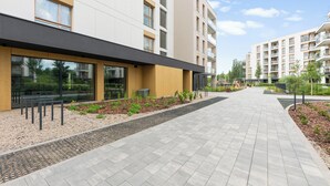 Edifici modern amb passeig pavimentat, grans finestres i teulada plana.