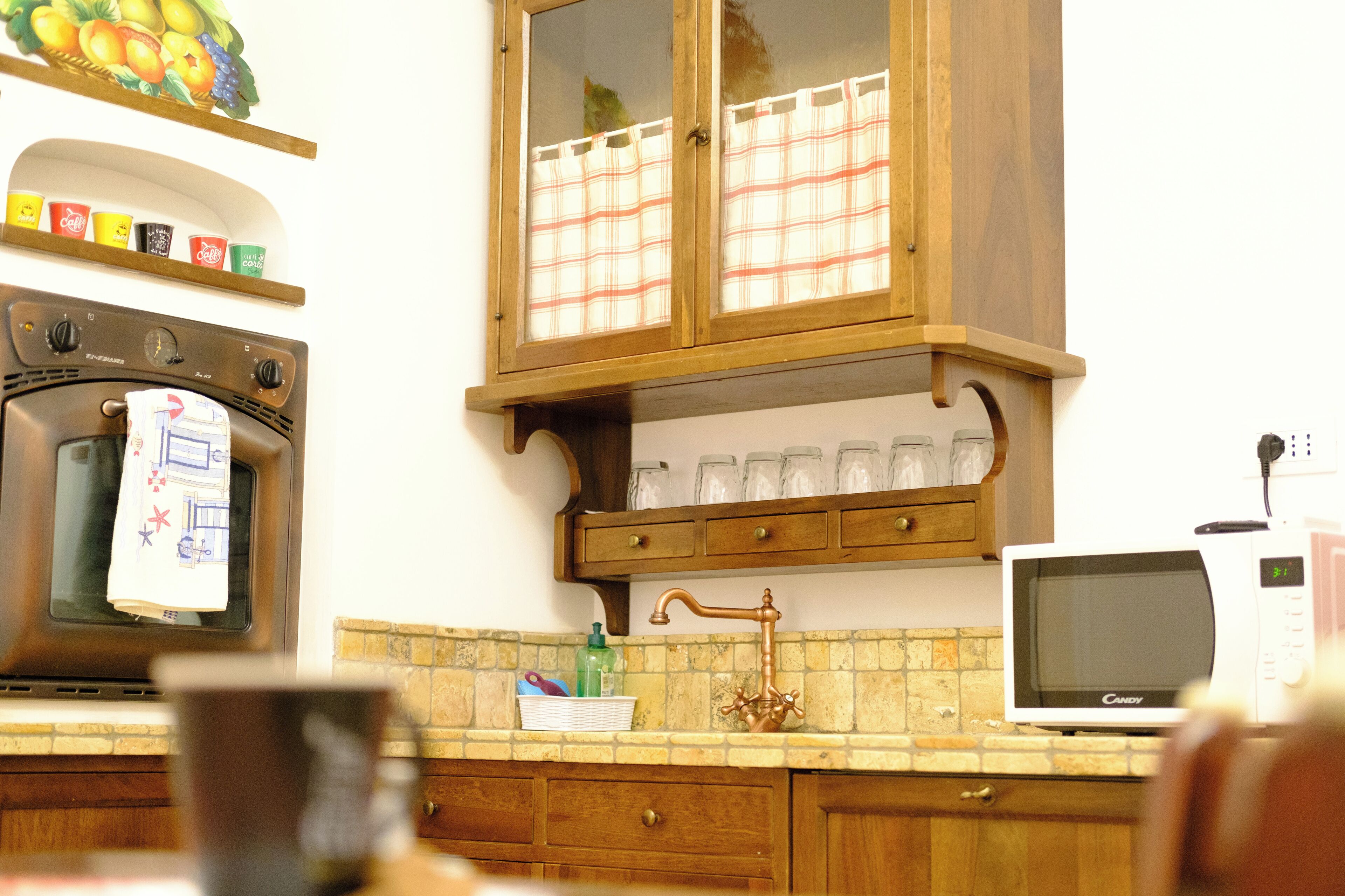 Una cocina con estufa, horno, microondas, armarios de madera y una ventana con cortina.