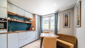 A modern kitchen with light blue cabinets, a wooden countertop, and a dining area with a table and chairs. - Apartment “Au Pied Des Pistes - Petit Châtel” with Mountain View, Private Terrace & Wi-Fi (Châtel)