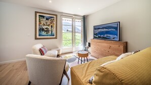 A spacious room with a large window, a sofa, a chair, and a television. - Apartment “Au Pied Des Pistes - Petit Châtel” with Mountain View, Private Terrace & Wi-Fi (Châtel)