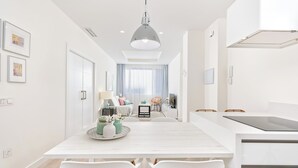 A modern kitchen with white cabinetry, a central island, and a dining area with a white table and chairs. - Solaga - Centro Alameda (Málaga)