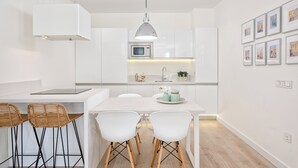 A modern kitchen with white cabinetry, a built-in microwave, a dining table with four chairs, and a pendant light. - Solaga - Centro Alameda (Málaga)