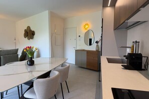 A modern kitchen with a coffee machine, a dining area with a table and chairs, and a living area with a sofa and a vase of flowers. - Casa dell'Avvocato by Studio Vita - Free Parking  (Bologna)