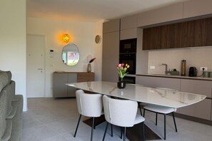 Una cucina moderna con un tavolo da pranzo in vetro, sedie bianche, un forno a microonde e una sveglia appesa al muro.