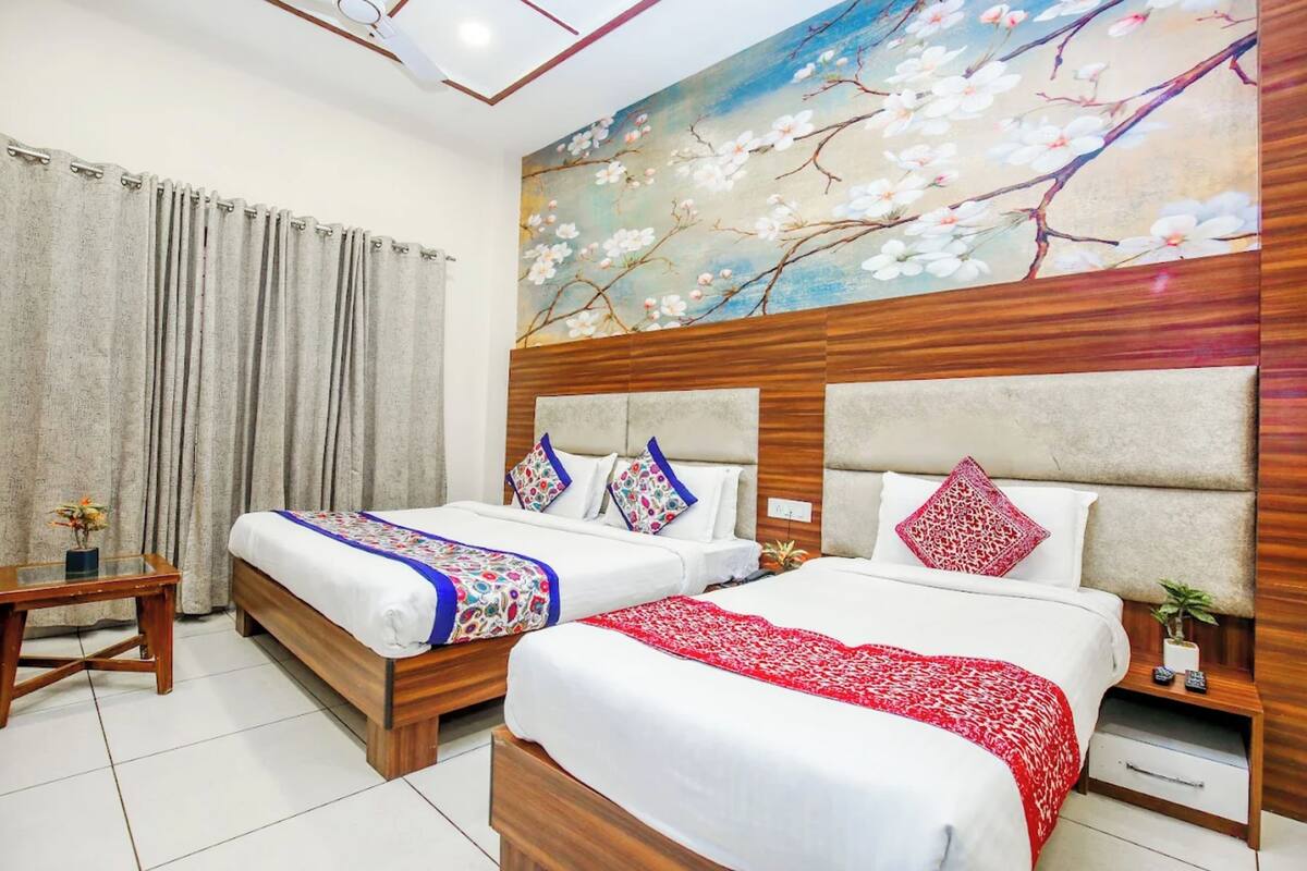 Ein Hotelzimmer mit zwei Betten, einem Holz-Kopfstück, einem Gemälde von Kirschblüten, einem kleinen Tisch und einem Nachttisch mit einer Pflanze.