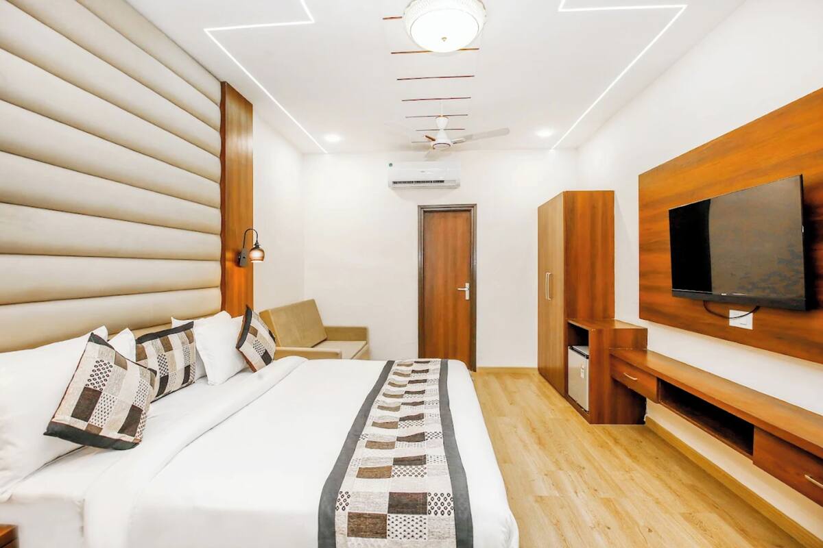Ein modernes Hotelzimmer mit einem großen Bett, einem Holzkopfende, integriertem Fernseher und einem Schrank aus Holz.