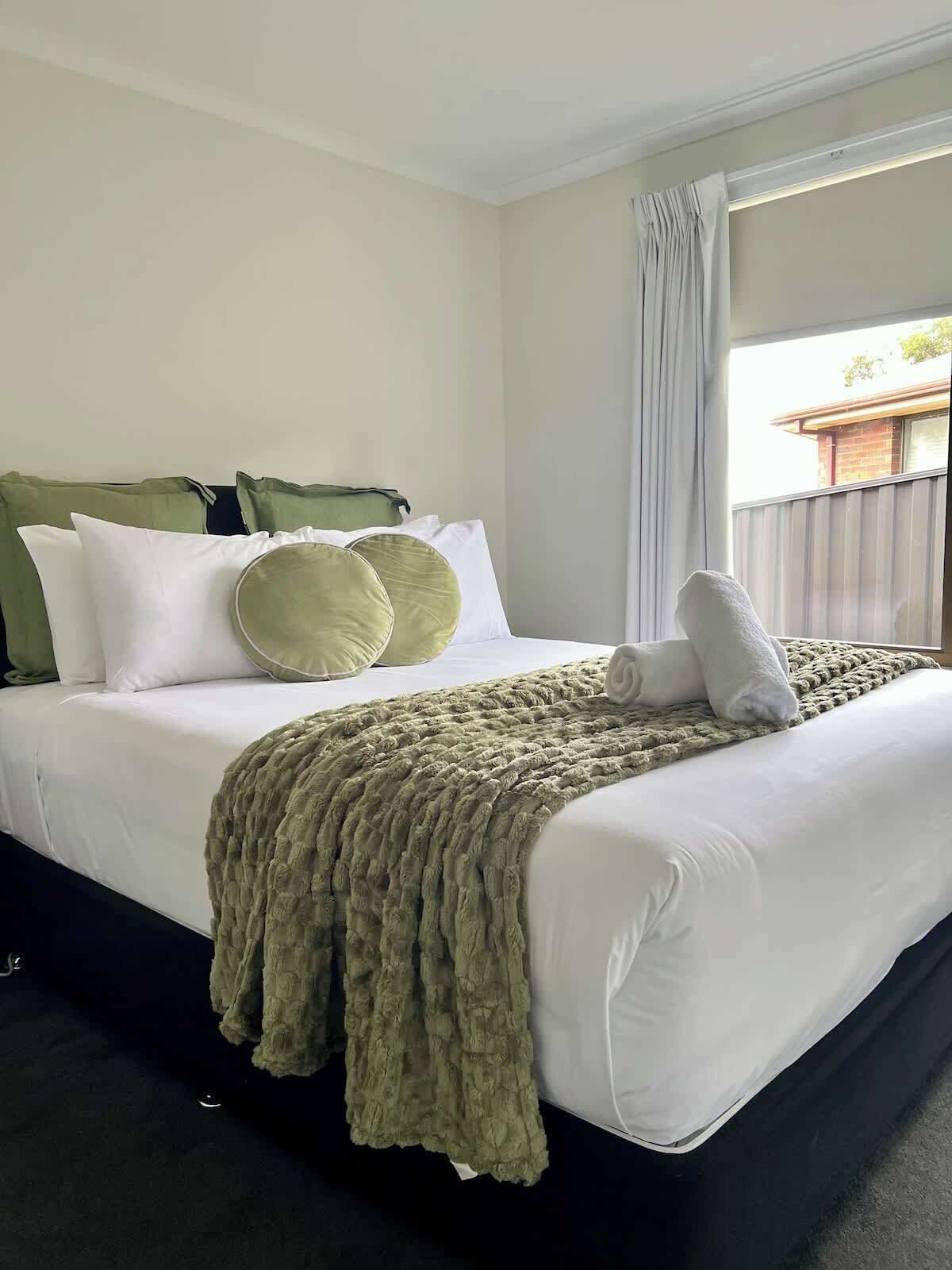 Quarto de hotel com cama, almofadas, cobertor e janela com cortinas.