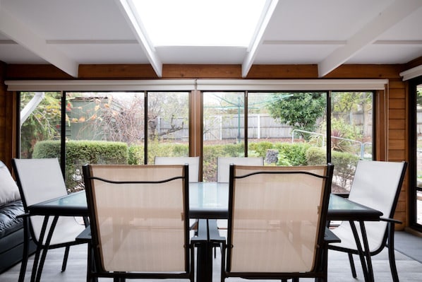 A dining area with a table and chairs, large windows, and a view of the garden.