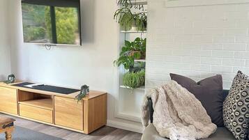 Uma sala de estar moderna com uma televisão de tela plana, um rack de madeira, um sofá redondo e uma estante para plantas.