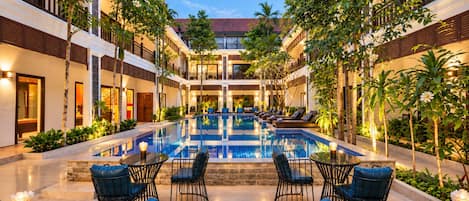 A hotel courtyard with a central swimming pool, lounge chairs, and tables.