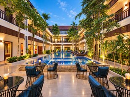 Un patio de hotel con piscina central, sillas de descanso y mesas.