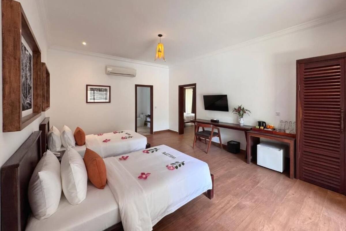 Ein Hotelzimmer mit zwei Betten, einem Schreibtisch, einem Fernseher und einer kleinen Kühlbox.