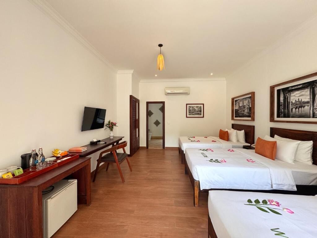 A hotel room with a desk, two beds, a TV, and artwork on the walls.