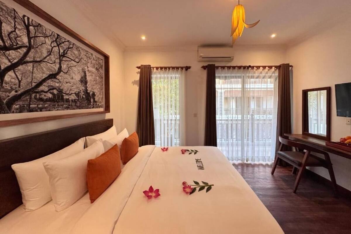 Ein Hotelzimmer mit Bett, Schreibtisch, Stuhl, einem Bild an der Wand und einem Fenster mit Vorhängen.