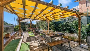 A covered patio area with a table and benches, surrounded by a wooden pergola and a green lawn. - Villa Talamone With Beautiful Sea View (Orbetello)