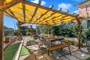 A covered patio area with a table and benches, surrounded by a wooden pergola and a green lawn. - Villa Talamone With Beautiful Sea View (Orbetello)