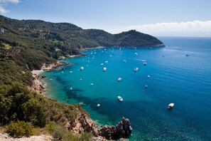 A coastal landscape with boats on clear blue water, rocky terrain, and dense greenery. - Villa Talamone With Beautiful Sea View (Orbetello)